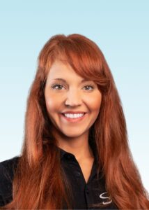 Smiling team member with long auburn hair wearing a black polo shirt