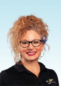 Smiling team member with curly hair, glasses, and a black polo shirt