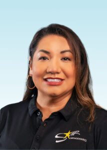 Smiling woman with long dark hair and hoop earrings wearing a black branded polo shirt