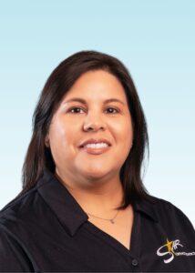 Smiling woman with long dark hair wearing a black embroidered polo shirt