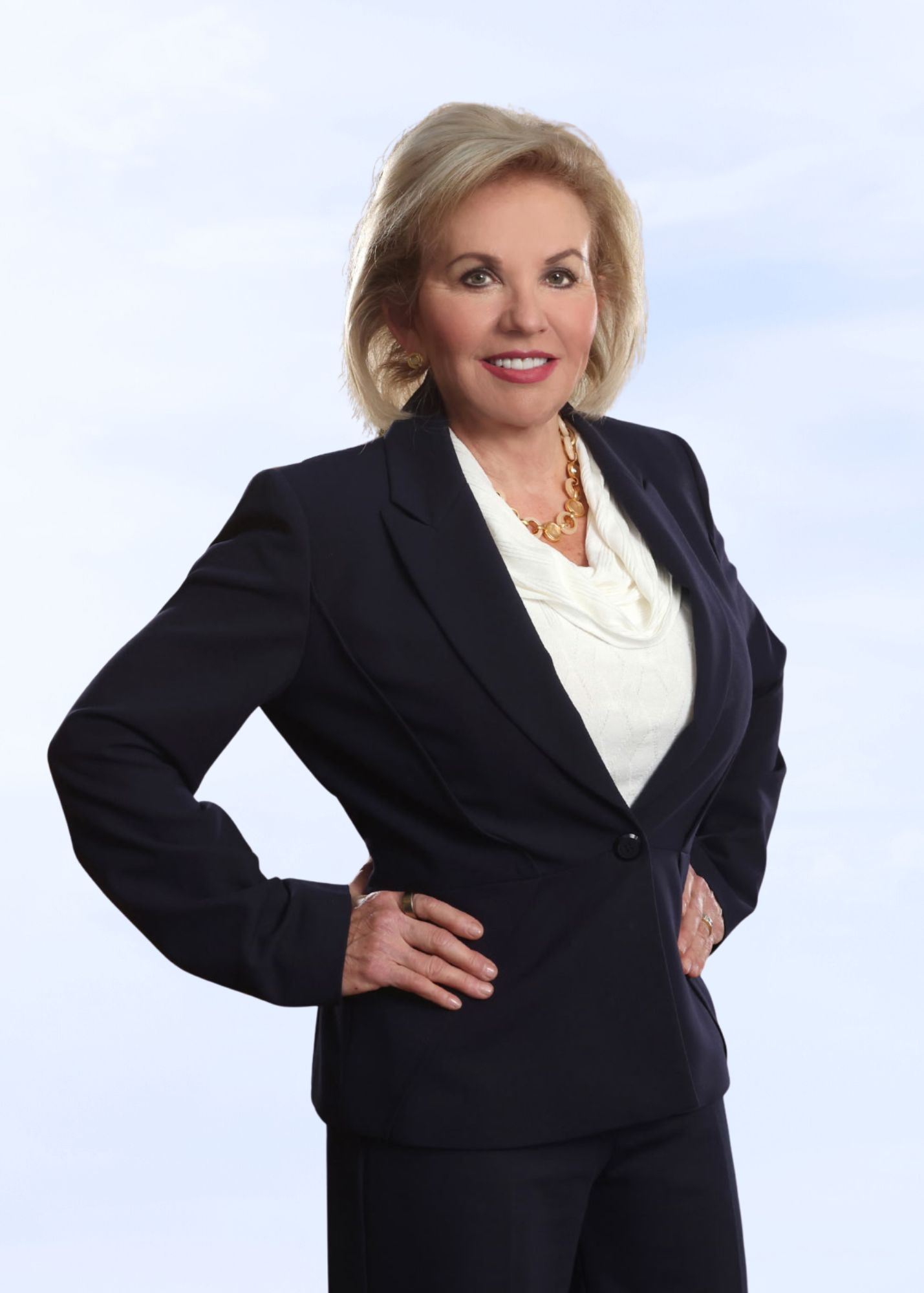 Smiling woman with blonde hair in navy blazer and white blouse, hands on hips