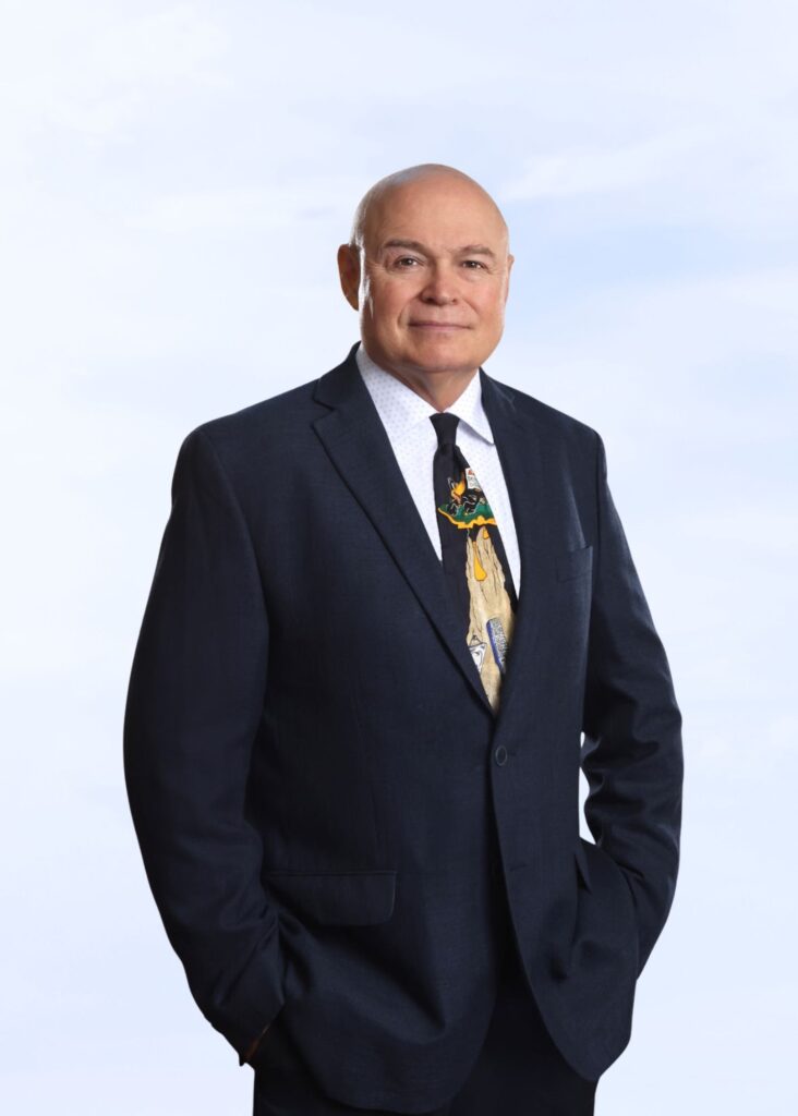 Smiling man in navy suit and novelty dental-themed tie, hands in pockets