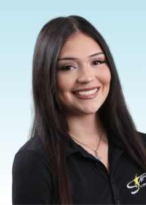 Smiling team member with long dark hair wearing a black embroidered polo shirt