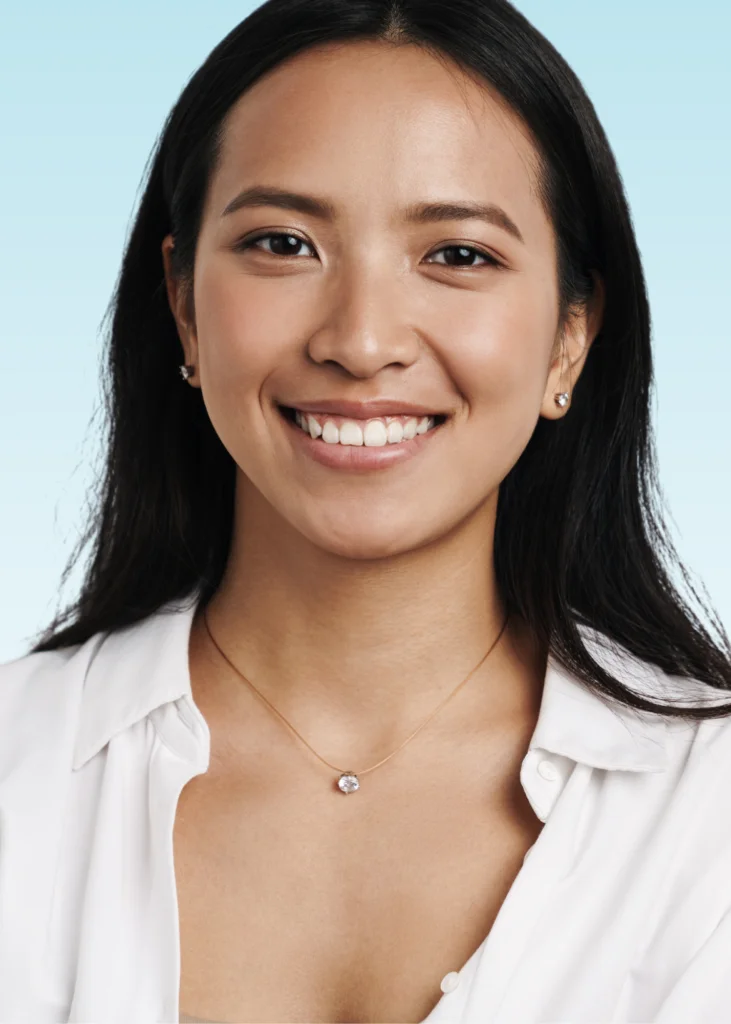 Smiling woman with long dark hair wearing a white blouse and necklace