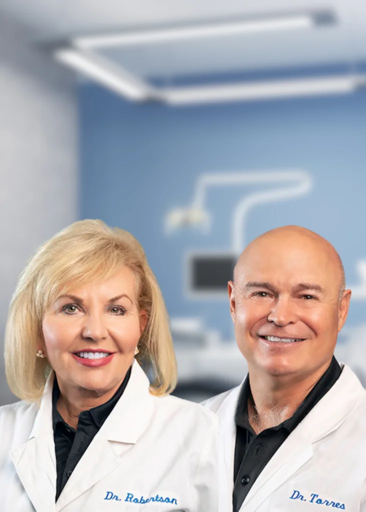 Dr. Robertson and Dr. Torres smiling in white coats inside a dental office