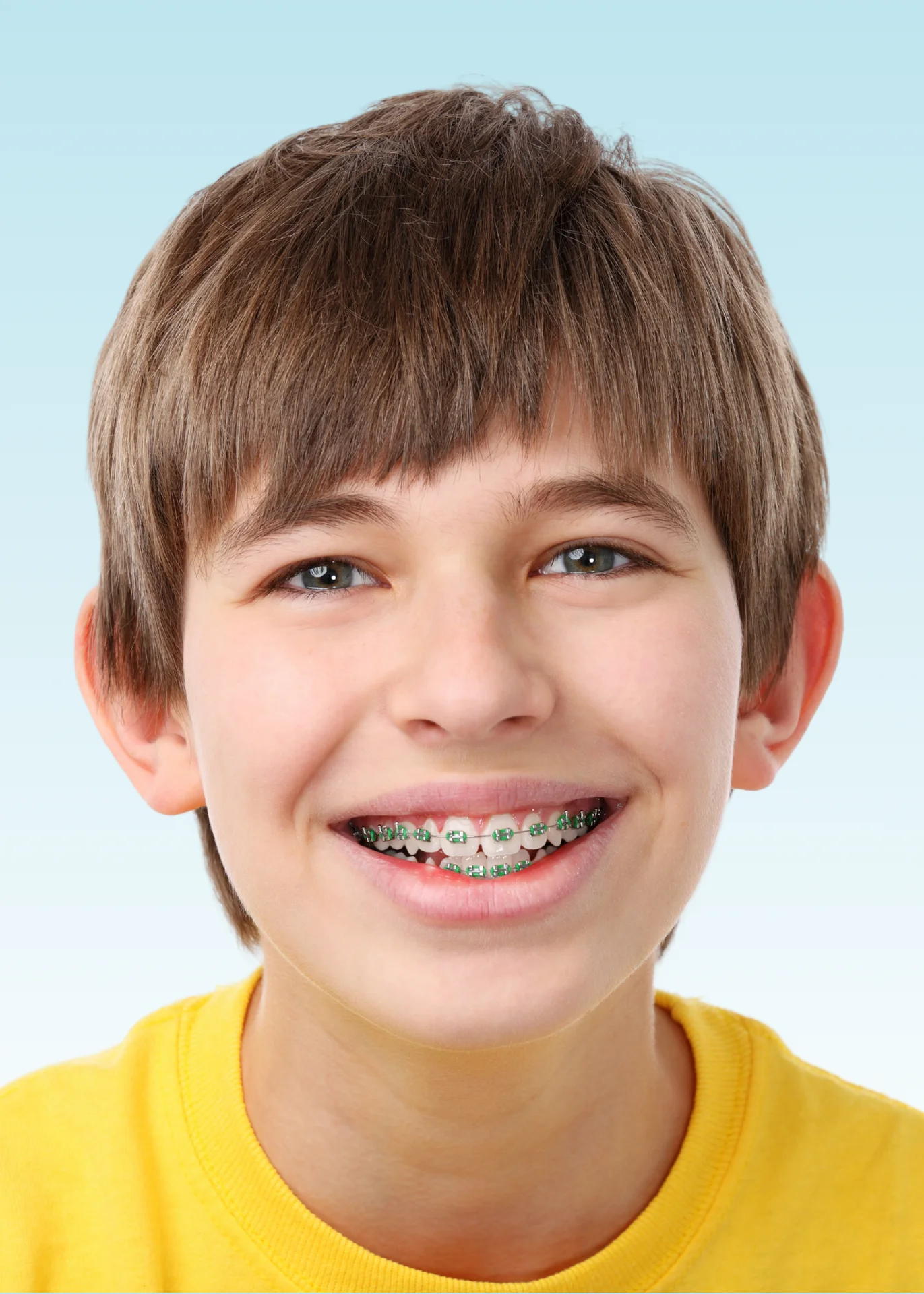 Smiling boy in yellow shirt with green metal braces on his teeth