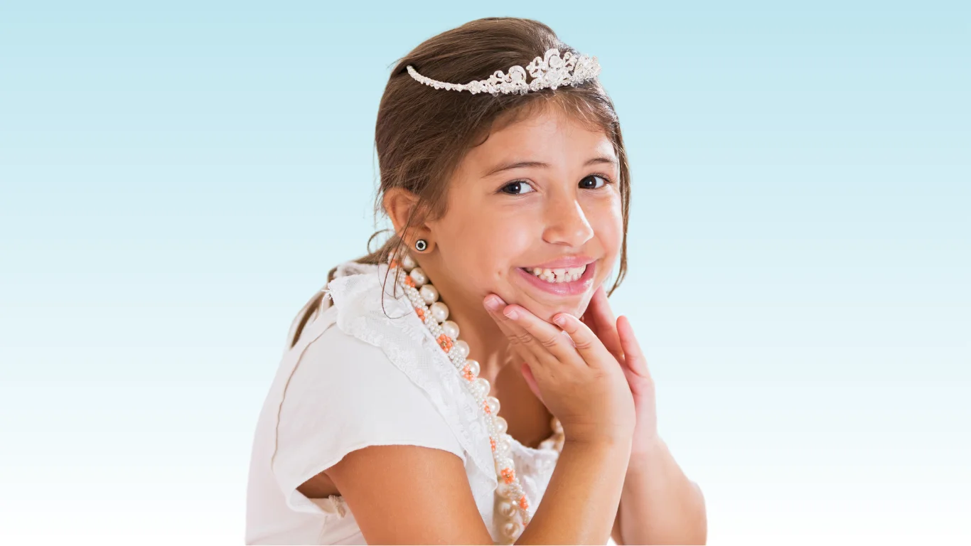 Smiling young girl wearing a tiara and pearl necklace, hand resting on chin