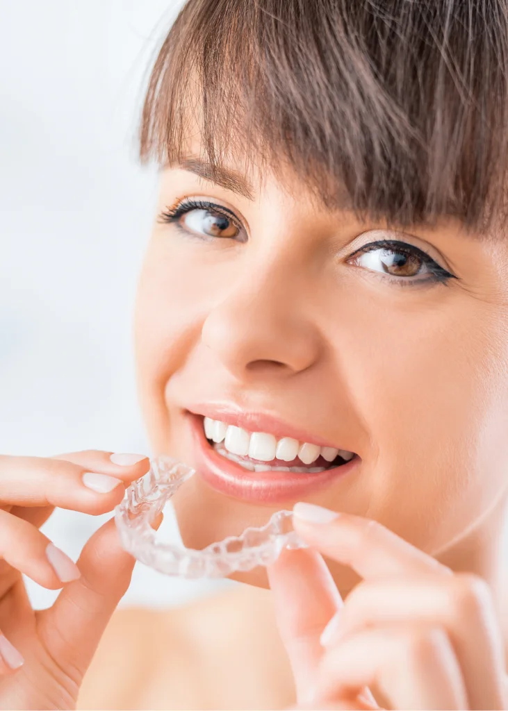 Smiling woman holding a clear aligner tray up to her teeth