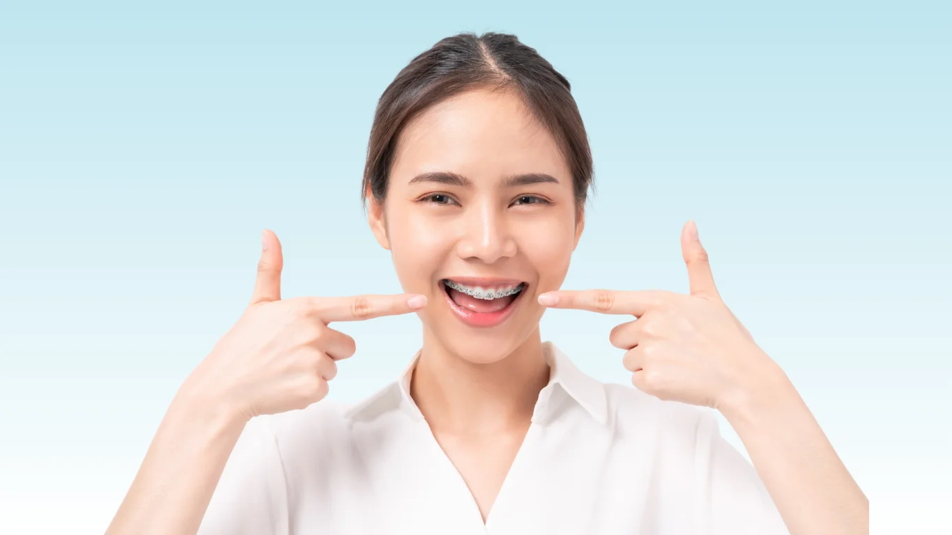 Smiling young woman pointing at her metal braces with both index fingers