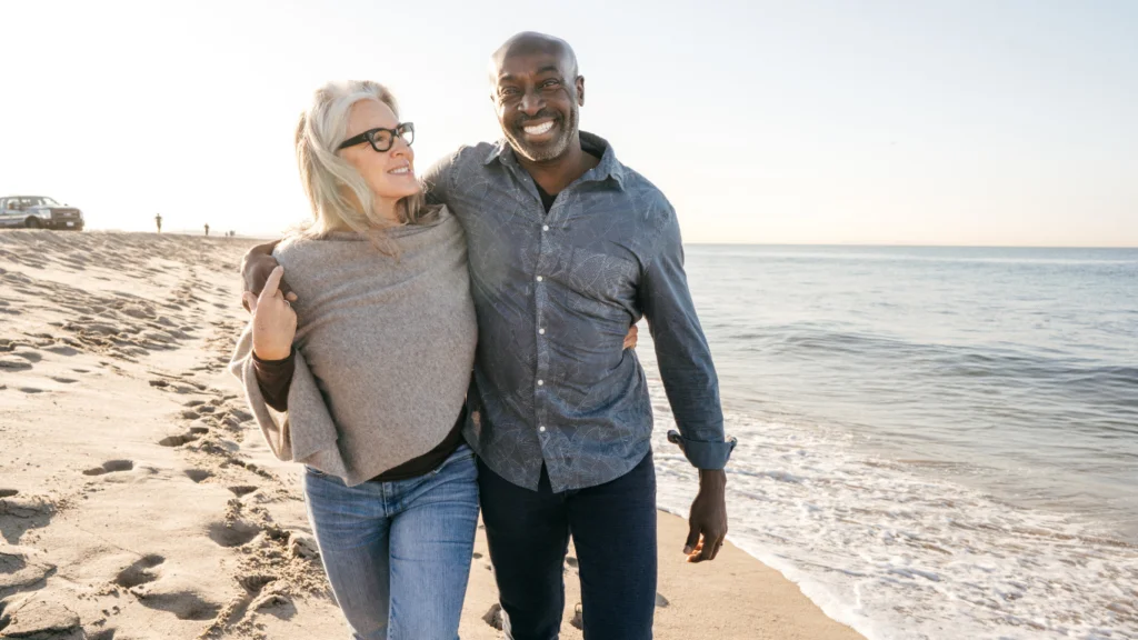 Smiling mature couple walking arm in arm along a sandy beach at sunset