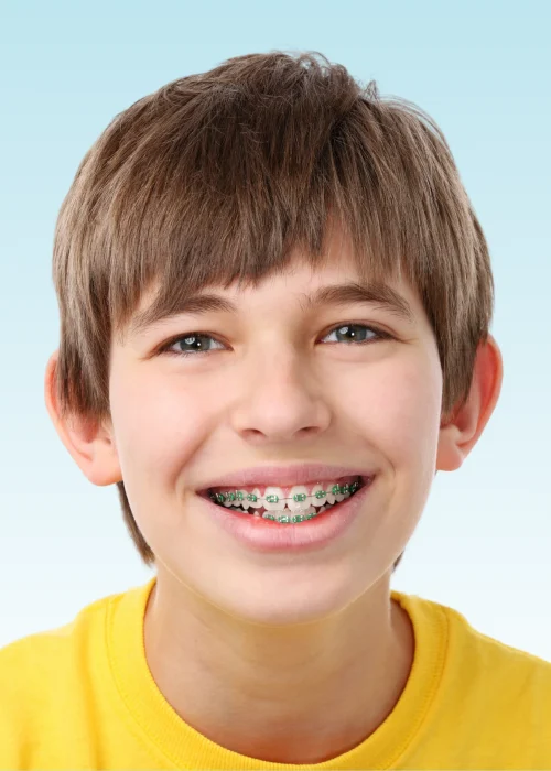 Smiling boy in yellow shirt with green metal braces on his teeth