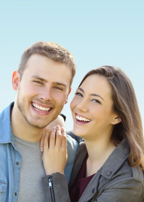 Smiling young couple showing bright white teeth against a light blue sky