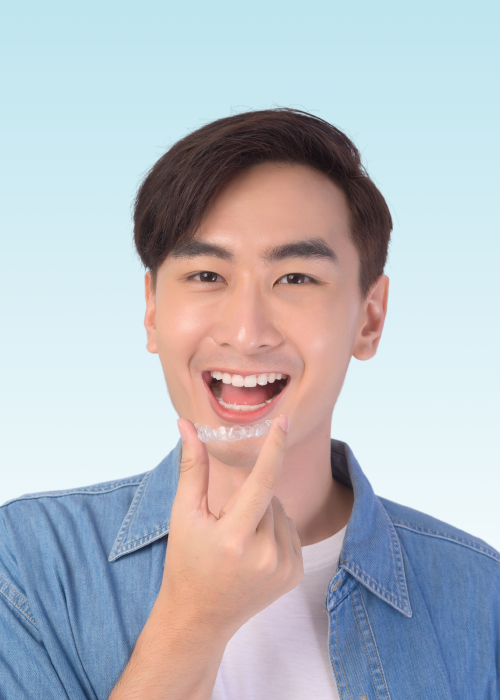 Smiling young man holding a clear aligner up to his teeth