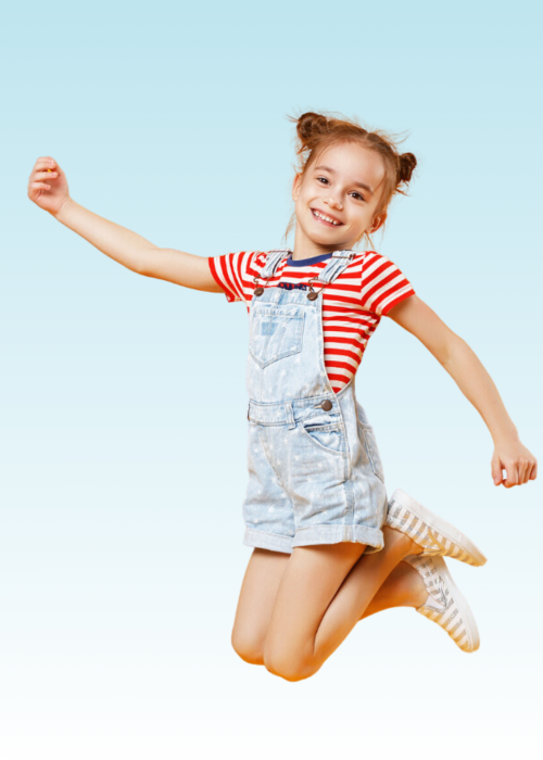 Smiling girl in denim overalls and striped shirt jumping joyfully in the air