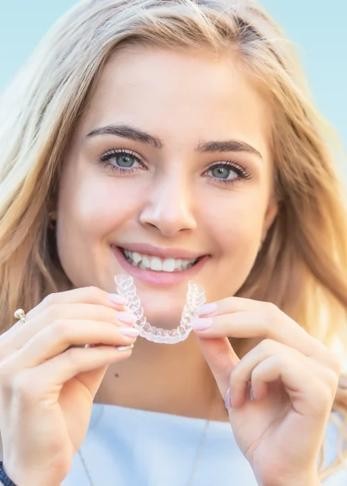 Smiling blonde teen holding a clear orthodontic aligner up to her mouth